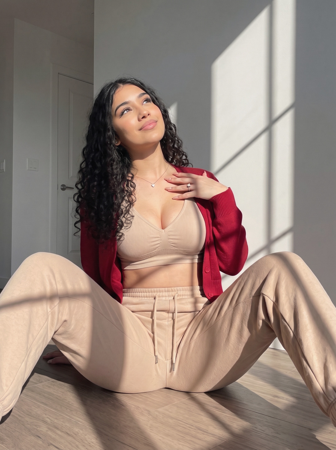 Mariana, con un cárdigan rojo y un conjunto beige, sentada al sol junto a una ventana.